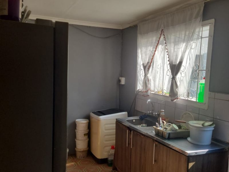 A functional scullery area featuring a stainless steel sink, tiled splashback, and window with security bars, providing a practical utility space.