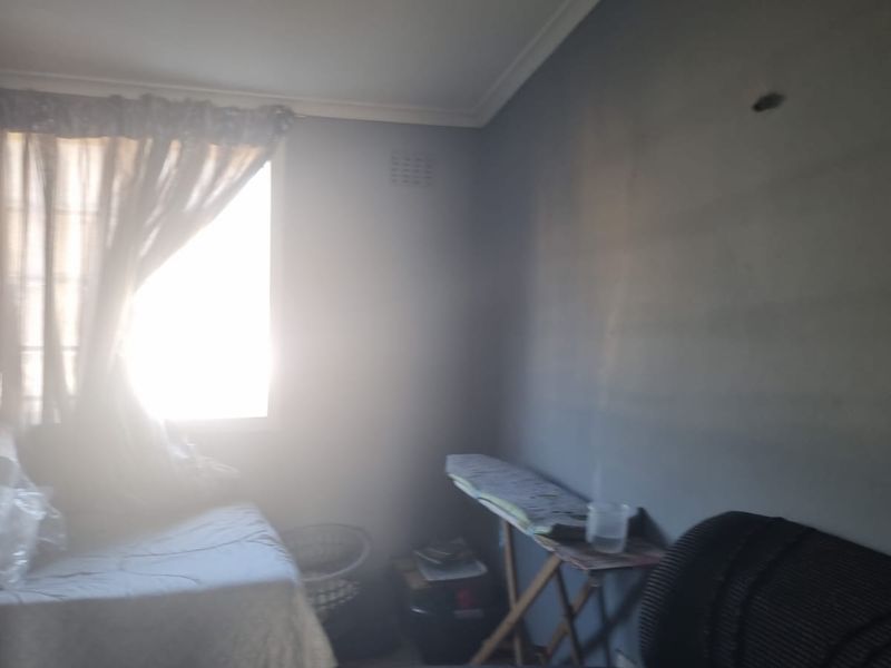 A bedroom featuring a window with curtains and wall-mounted ventilation, currently showing signs of wear and surface staining.