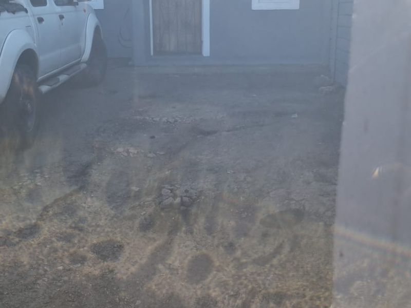 Front elevation of a residential property featuring a security gate and a driveway in need of significant repair and resurfacing.