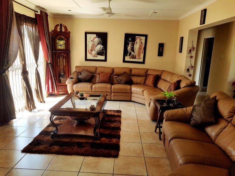 A spacious living room featuring tiled flooring, a ceiling fan, and large sliding glass doors with security gates providing access to the exterior.