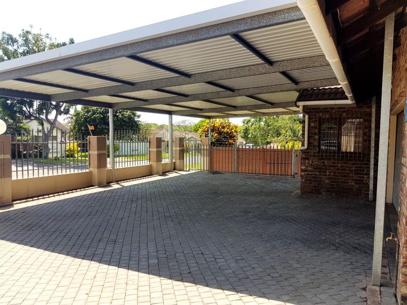 A spacious, paved carport area featuring a sturdy metal roof structure, brick perimeter walls, and secure steel fencing.