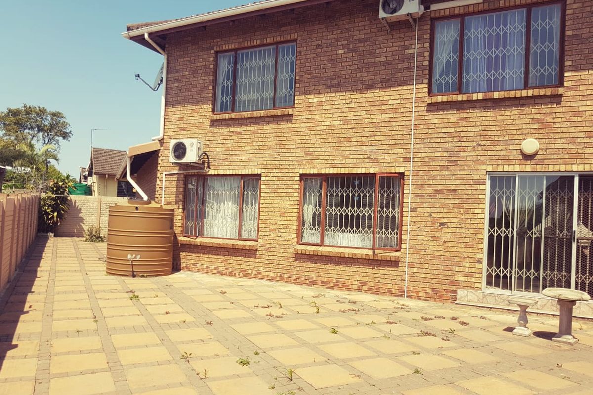 Rear exterior view of a double-story brick house featuring a paved patio area, security bars on windows, and an installed water storage tank.
