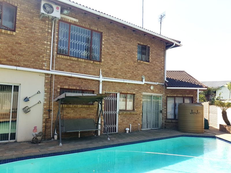 Rear exterior view of a brick house featuring a swimming pool, paved patio area, and a water storage tank.