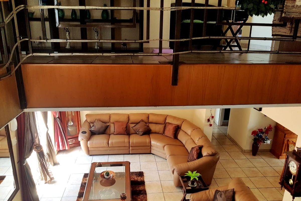 Spacious open-plan living area featuring a mezzanine level with metal balustrade, tiled flooring, and warm wooden accents.