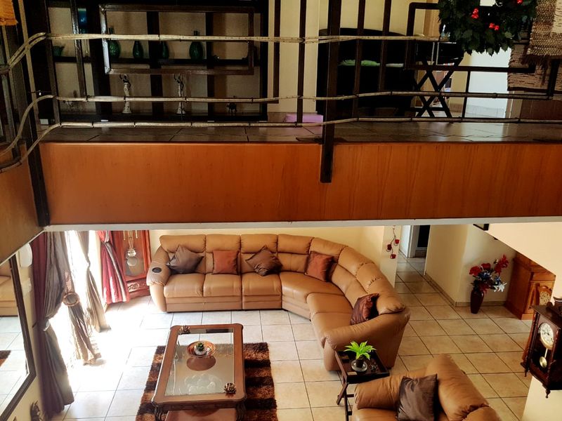 Spacious open-plan living area featuring a mezzanine level with metal balustrade, tiled flooring, and warm wooden accents.