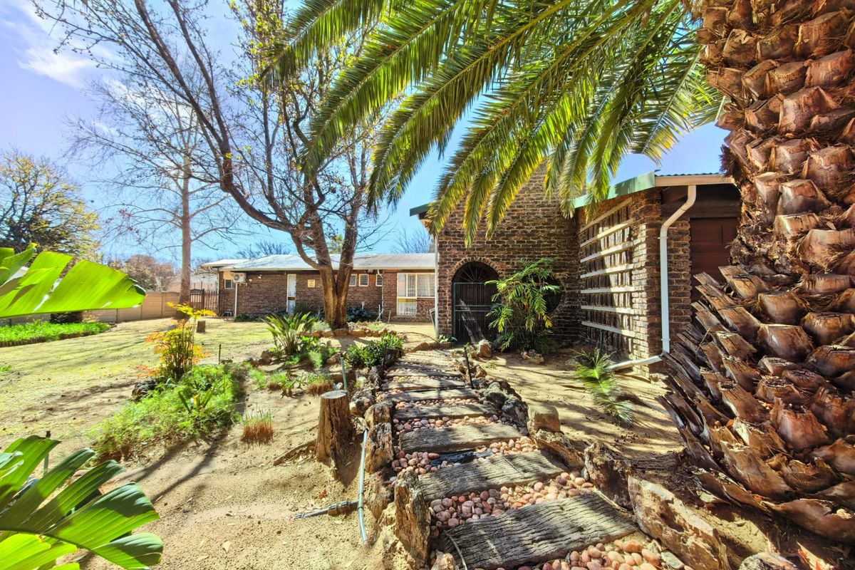 A view of the rear exterior featuring a brick facade, a stone-paved garden path, and established landscaping with mature trees.