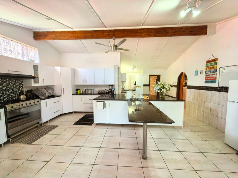 Spacious kitchen featuring white cabinetry, granite countertops, a central island, gas stove, and an exposed timber beam ceiling.