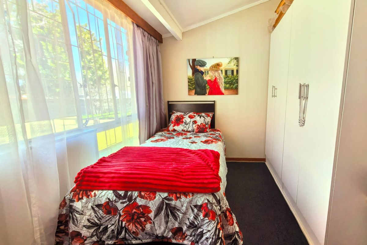 A functional bedroom featuring built-in cupboards, carpeted flooring, and a large window allowing for natural light.