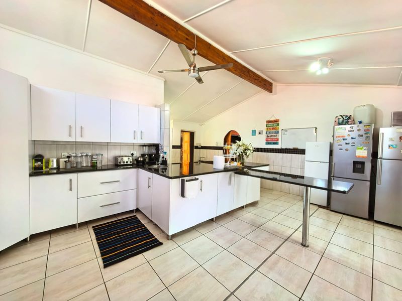 Spacious kitchen featuring white cabinetry, black granite countertops, a breakfast bar, exposed timber ceiling beam, and tiled flooring.