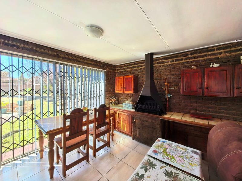 Living area featuring exposed brick walls, built-in indoor braai, tiled flooring, and sliding door access to the garden.