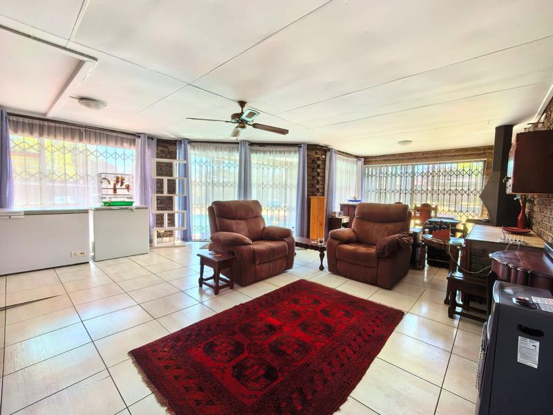 Spacious living room featuring tiled flooring, exposed brick walls, a built-in fireplace, and large windows with security gates.