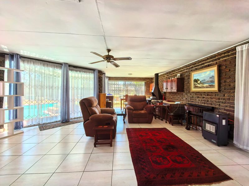 Spacious living room featuring an exposed brick wall, built-in fireplace, tiled flooring, and large sliding glass doors providing access to the pool area.