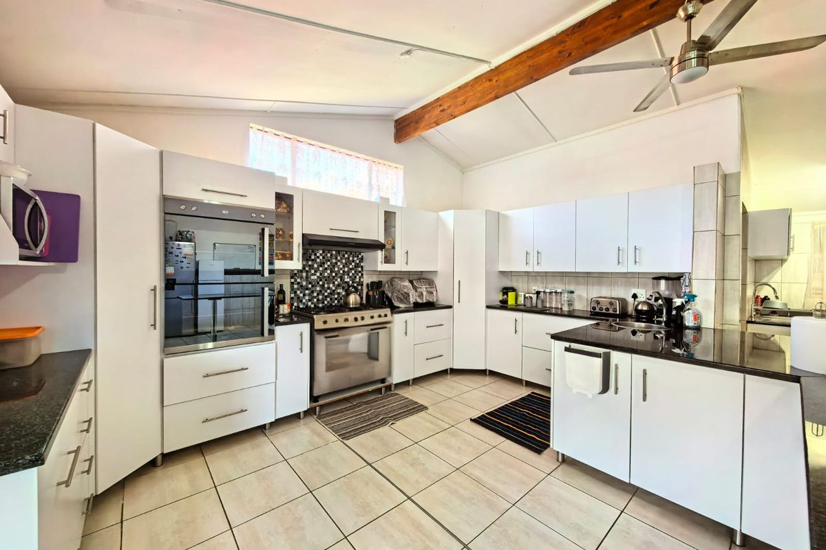 Spacious kitchen featuring white cabinetry, granite countertops, a built-in oven, gas hob, and an exposed timber ceiling beam with tiled flooring throughout.