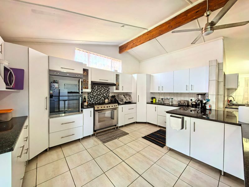Spacious kitchen featuring white cabinetry, granite countertops, a built-in oven, gas hob, and an exposed timber ceiling beam with tiled flooring throughout.