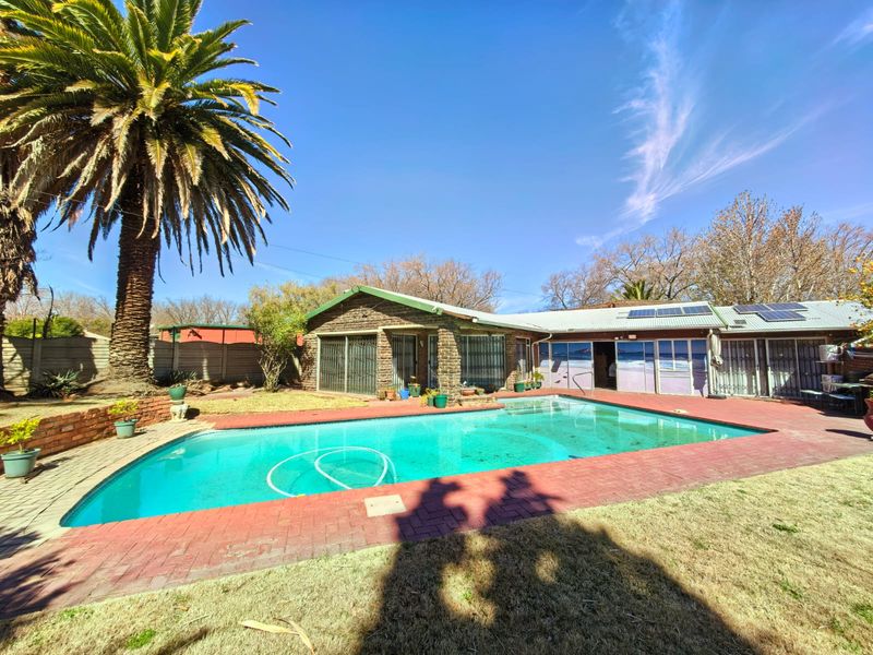 Rear exterior view featuring a swimming pool, brick paved surround, and solar panels installed on the roof.