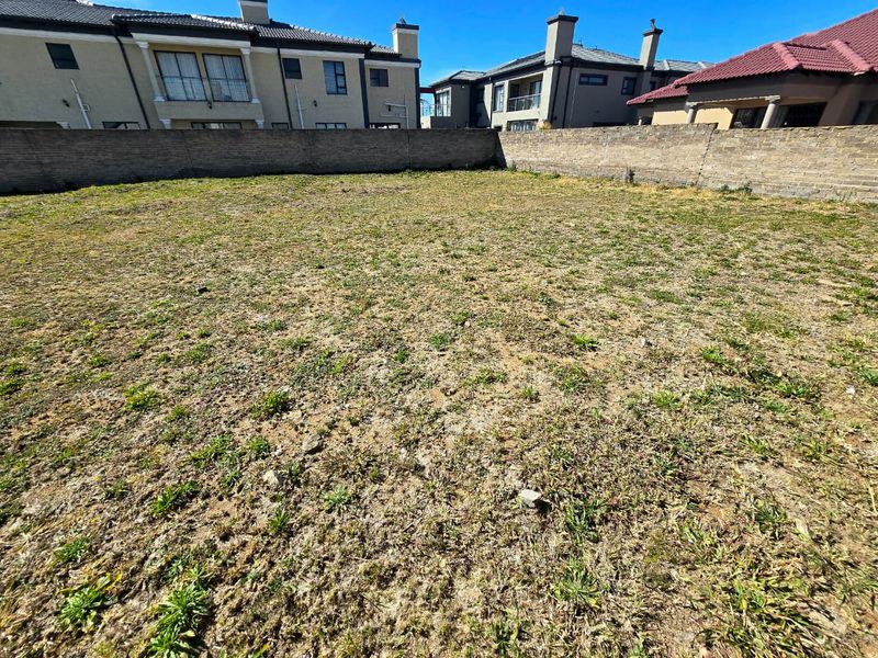 A vacant residential plot featuring a level grassed area enclosed by a perimeter brick wall, situated within a developed residential estate.
