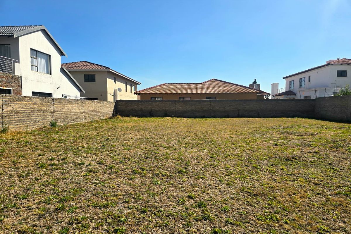 A vacant residential plot featuring level ground and enclosed by a perimeter brick wall, situated within an established neighborhood.