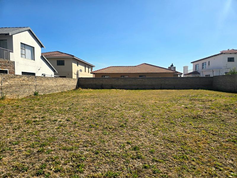 A vacant residential plot featuring level ground and enclosed by a perimeter brick wall, situated within an established neighborhood.