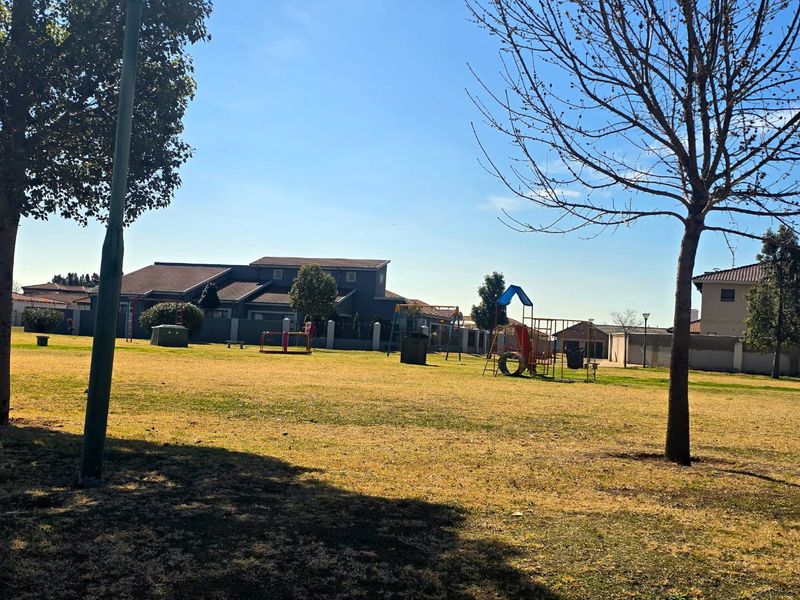 A spacious residential garden area featuring a playground set, mature trees, and perimeter walling within a well-maintained estate setting.