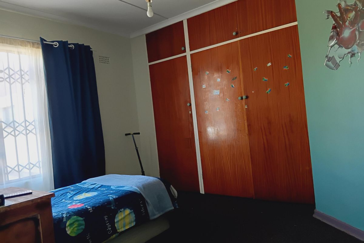 A bedroom featuring built-in wooden cupboards and a window fitted with a security gate.