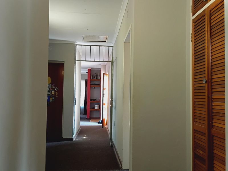A functional hallway featuring built-in wooden louvered storage cupboards and carpeted flooring, leading towards an additional interior space.
