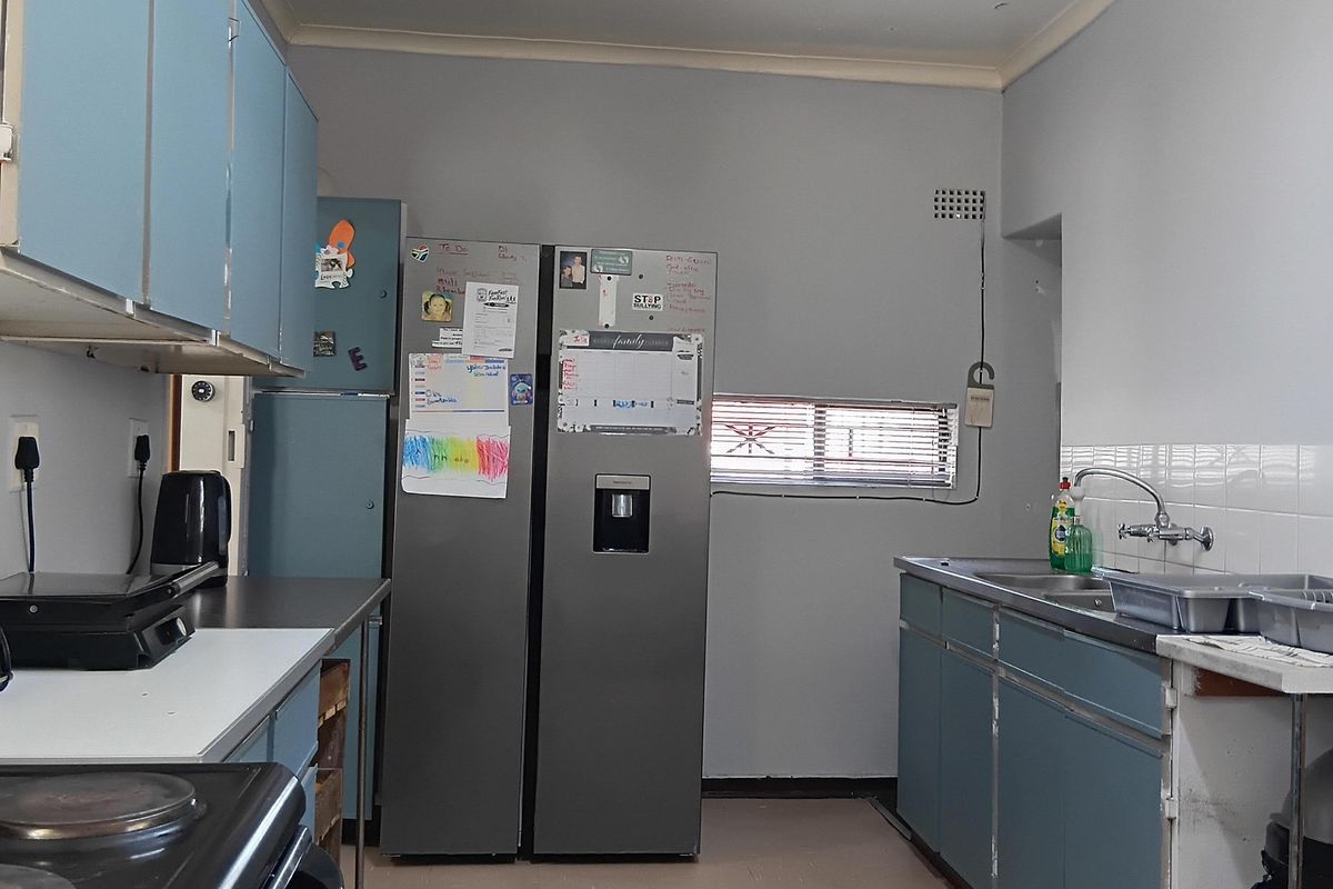 A functional kitchen featuring blue cabinetry, a stainless steel sink, and an electric stove, offering a dated aesthetic with potential for modernization.