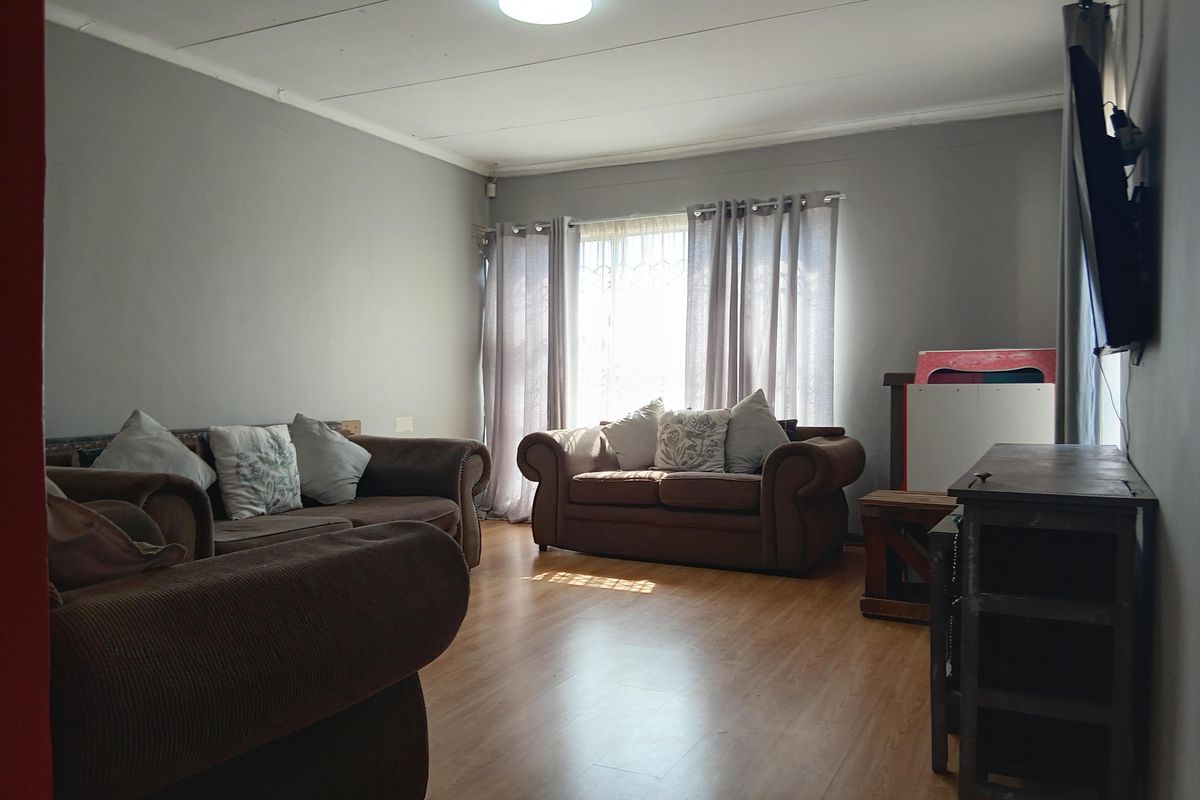A living room featuring laminate flooring, neutral wall tones, and a window fitted with security bars, providing a functional and well-lit space.