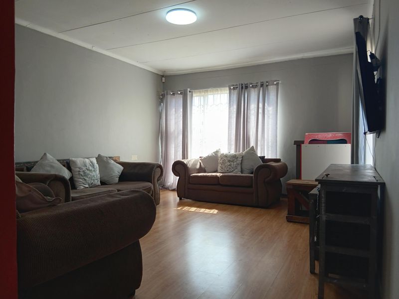 A living room featuring laminate flooring, neutral wall tones, and a window fitted with security bars, providing a functional and well-lit space.