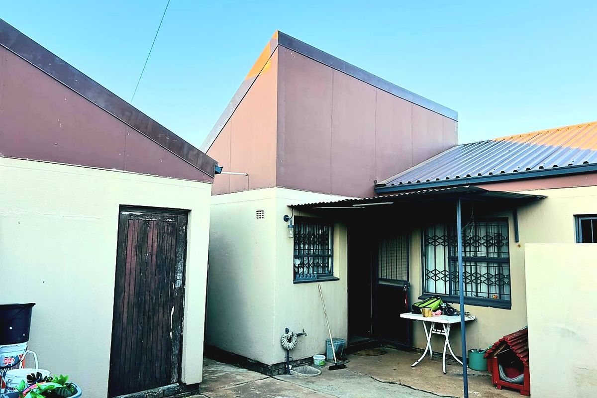 Rear exterior view of the property featuring a concrete patio area, metal roofing, and security gates on windows.