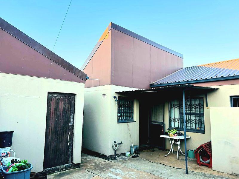 Rear exterior view of the property featuring a concrete patio area, metal roofing, and security gates on windows.