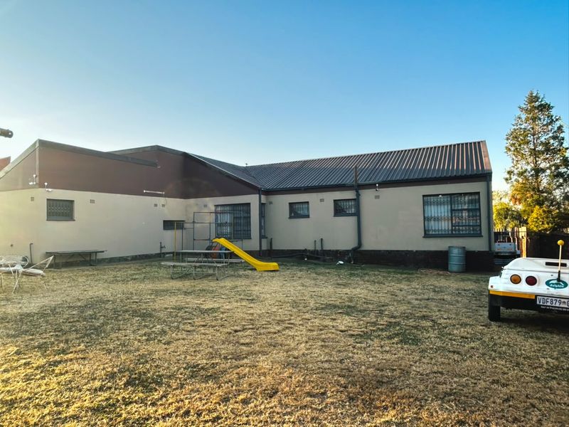 Rear view of the property featuring a large garden area, metal roofing, and security bars on the windows.