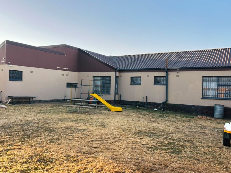 Rear view of the property featuring a large backyard, metal security bars on windows, and a corrugated metal roof.