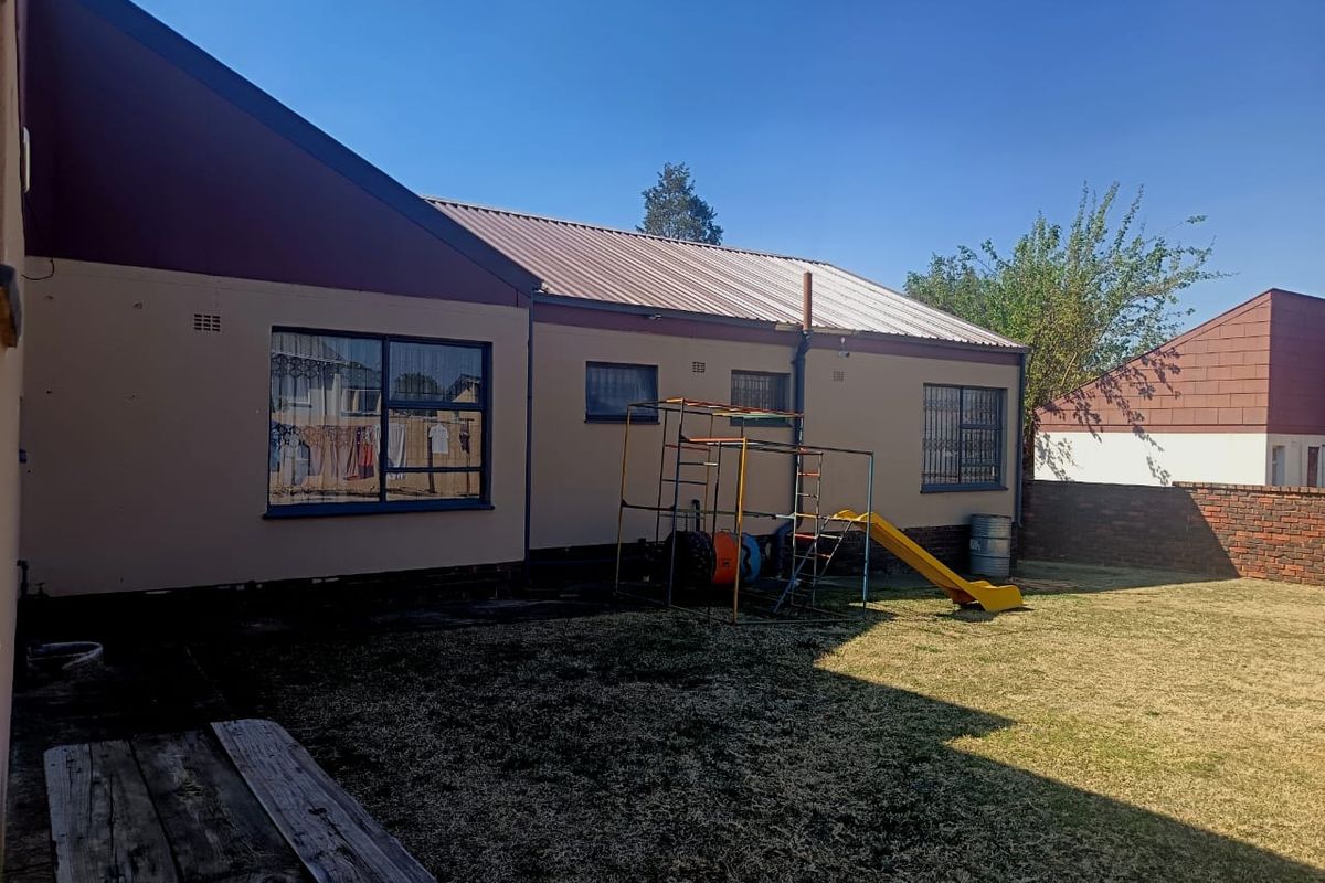 Rear view of the property featuring a metal roof, security bars on windows, and a private garden area with a brick boundary wall.