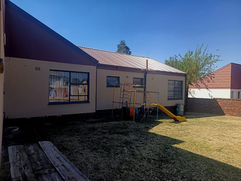 Rear view of the property featuring a metal roof, security bars on windows, and a private garden area with a brick boundary wall.