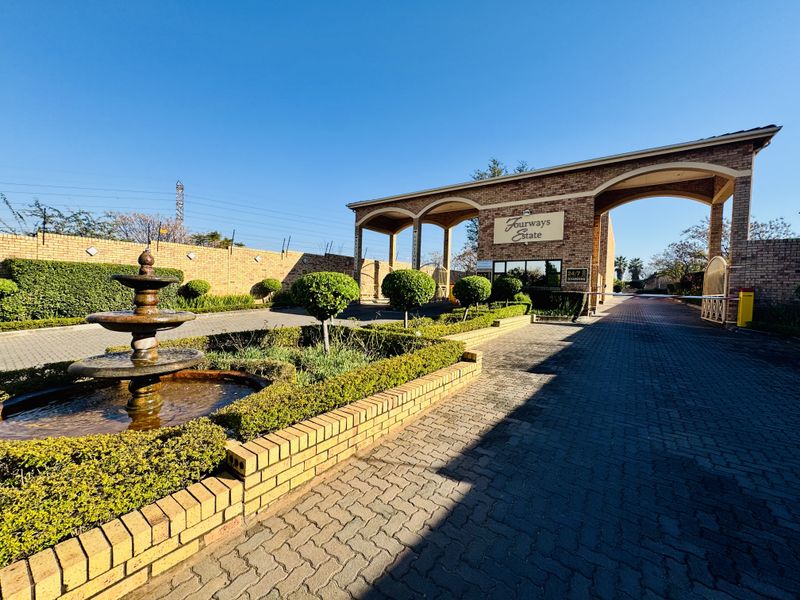 The entrance to Fourways Estate featuring a brick security gatehouse, paved driveway, landscaped garden, and a decorative water fountain.