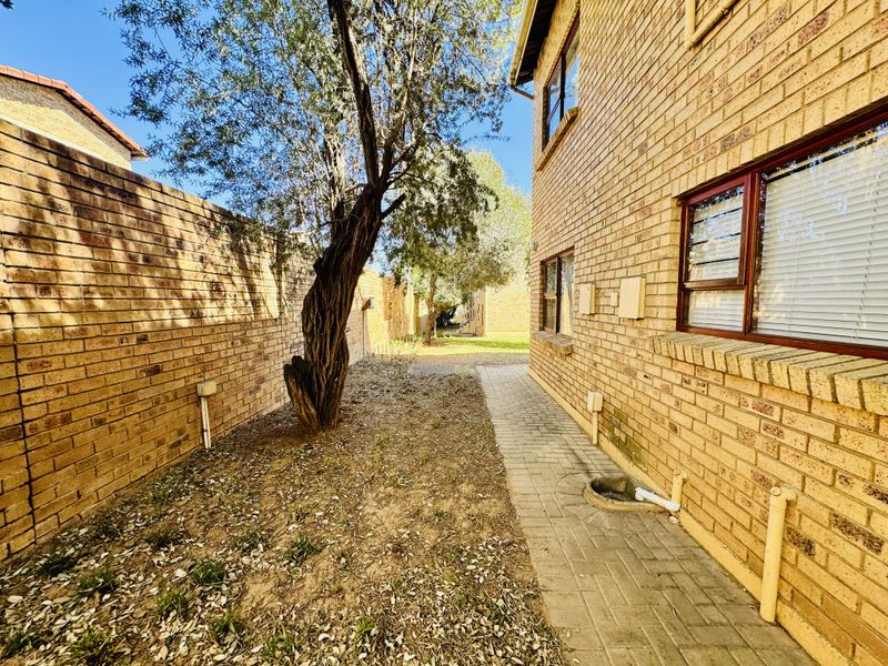 Rear exterior view of the flat featuring a paved walkway, face brick facade, and a side garden area requiring maintenance.