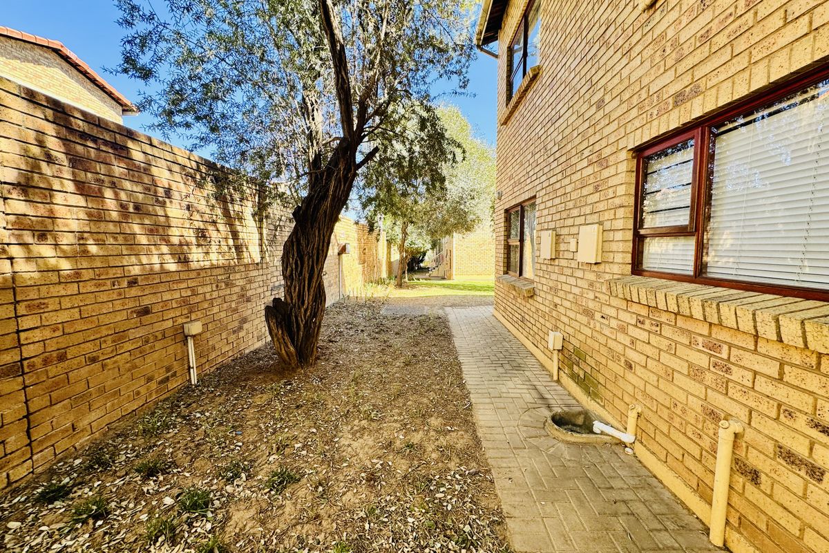 Rear exterior view of the flat featuring a paved walkway, face brick facade, and a side garden area requiring maintenance.