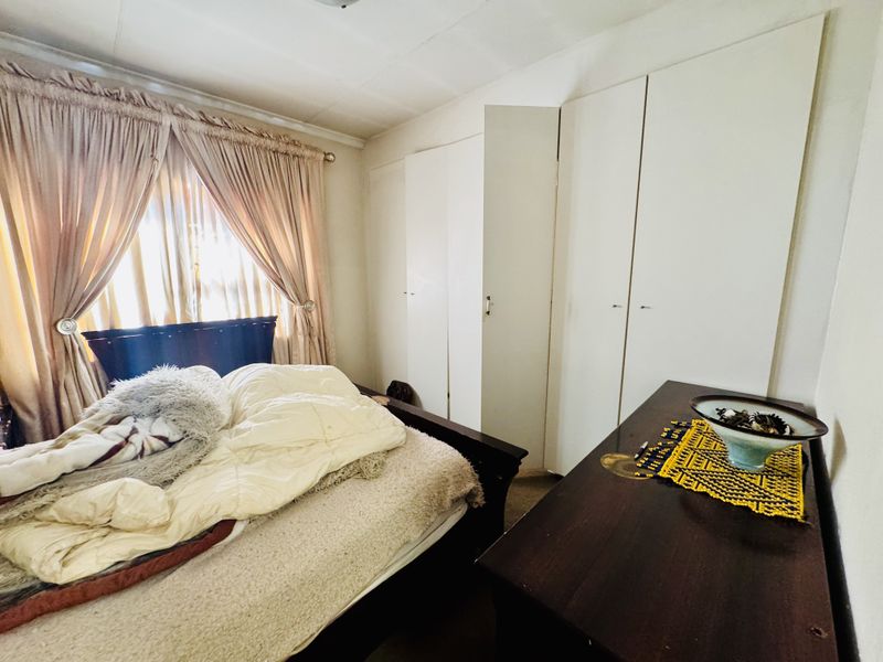 A bedroom featuring built-in cupboards and natural light, requiring cosmetic updates to the ceiling and finishes to enhance its appeal.