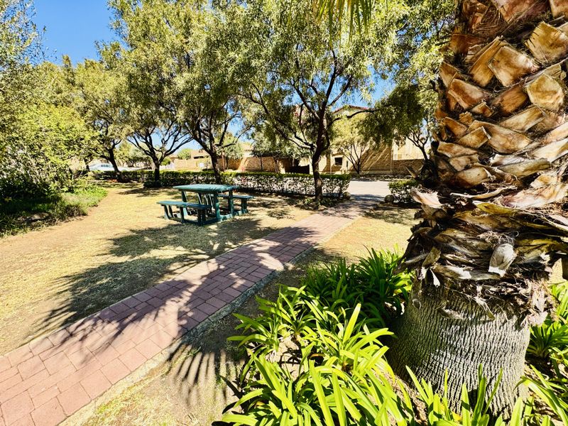 A well-maintained communal garden area featuring mature trees, established landscaping, and a paved brick walkway.