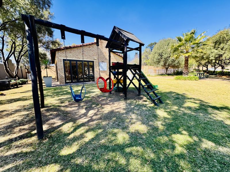 A well-maintained garden area featuring a lawn, mature trees, and a brick-built residential structure with sliding glass doors.