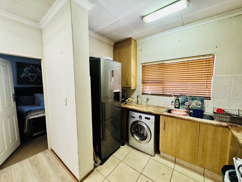 Compact kitchen featuring laminate cabinetry, granite countertops, and integrated laundry plumbing, with a view into the adjacent bedroom.