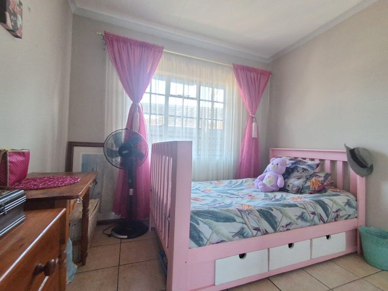 A bedroom featuring tiled flooring and a window fitted with security burglar bars.