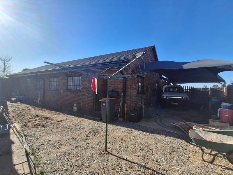 Rear view of the brick house featuring a tiled roof, security bars on windows, and a covered carport area.