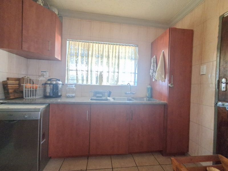 A functional kitchen featuring laminate cabinetry, tiled backsplash, and tiled flooring, offering a practical layout with potential for modern cosmetic updates.