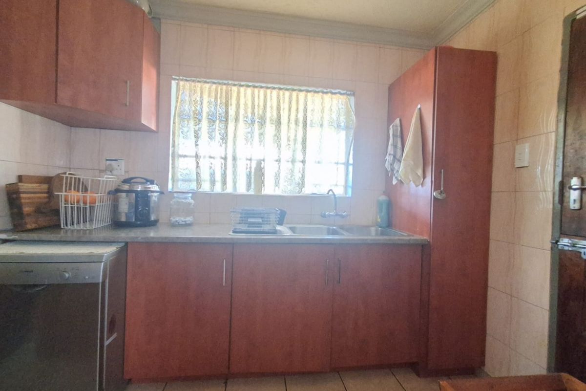A functional kitchen featuring laminate cabinetry, tiled backsplash, and tiled flooring, offering a practical layout with potential for modern cosmetic updates.
