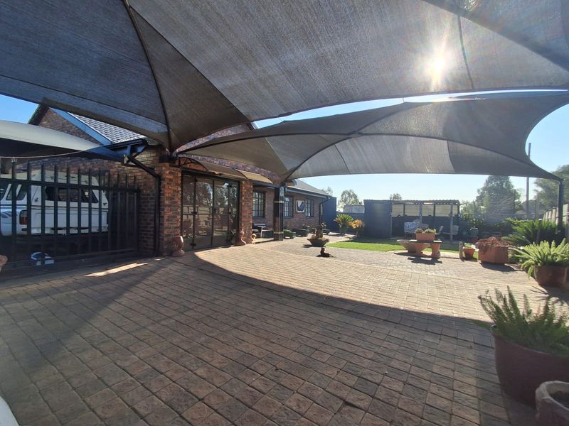 A spacious paved outdoor patio area featuring a large overhead shade sail, brick exterior walls, and secure metal gate access.