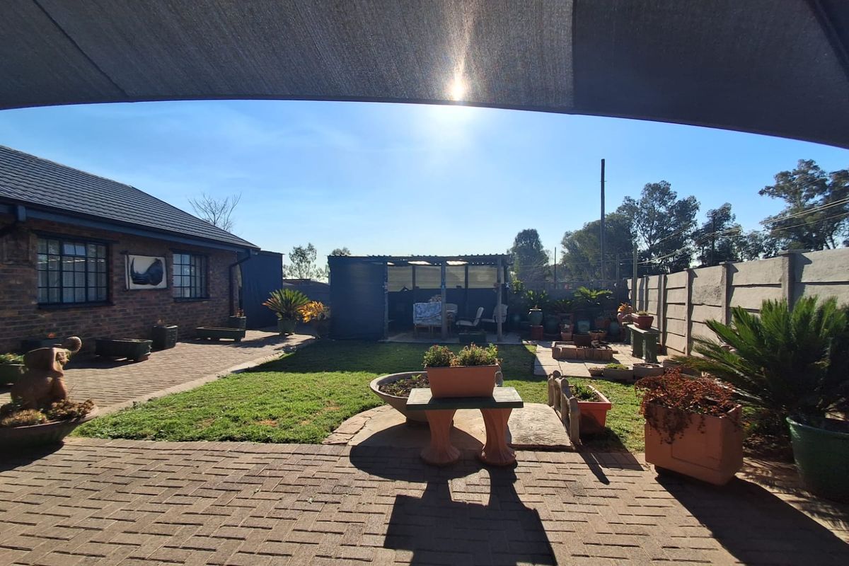 A rear garden area featuring brick paving, a lawn, and a precast concrete boundary wall, viewed from under a shade sail.