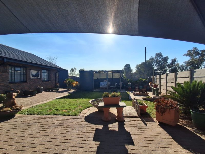 A rear garden area featuring brick paving, a lawn, and a precast concrete boundary wall, viewed from under a shade sail.