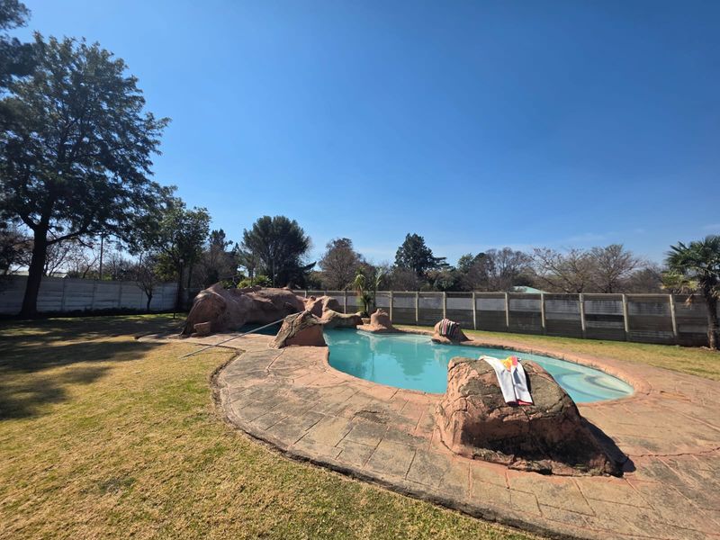 Outdoor swimming pool area featuring a naturalistic rock design, paved surround, and perimeter wall in a spacious garden setting.