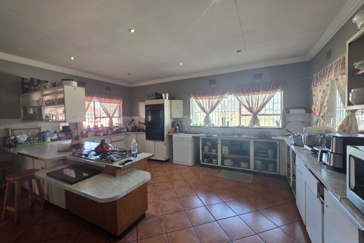 Spacious kitchen featuring a central island with gas hob, built-in oven, double sink, and ample cabinetry, finished with tiled flooring and recessed lighting.